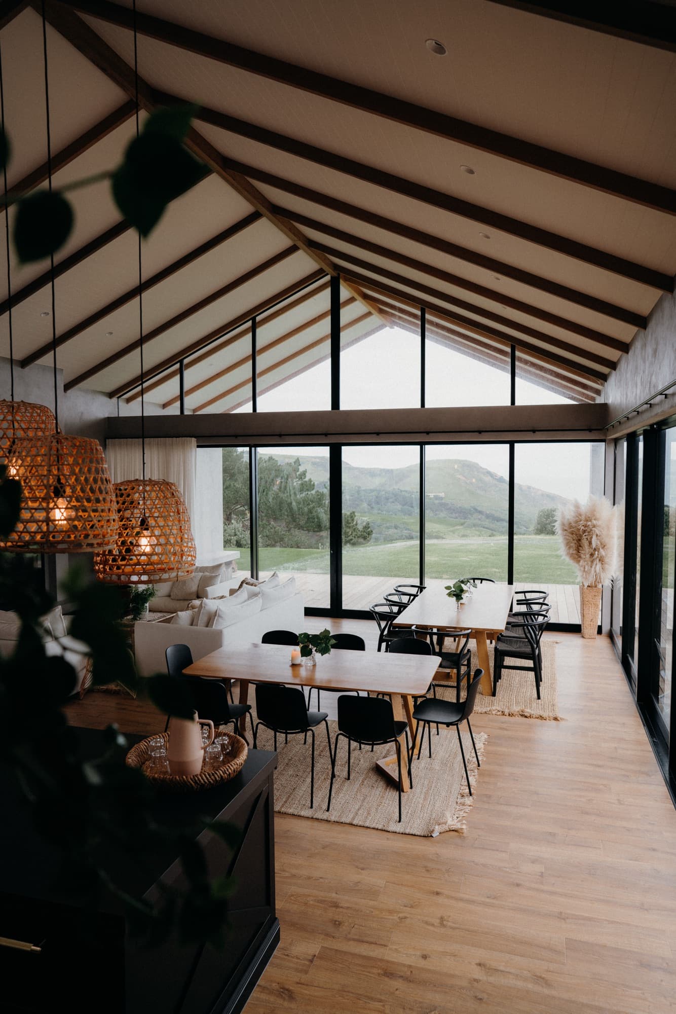 The light-filled gathering room at Kula Muriwai, long tables set beneath a vaulted ceiling with the hills beyond
