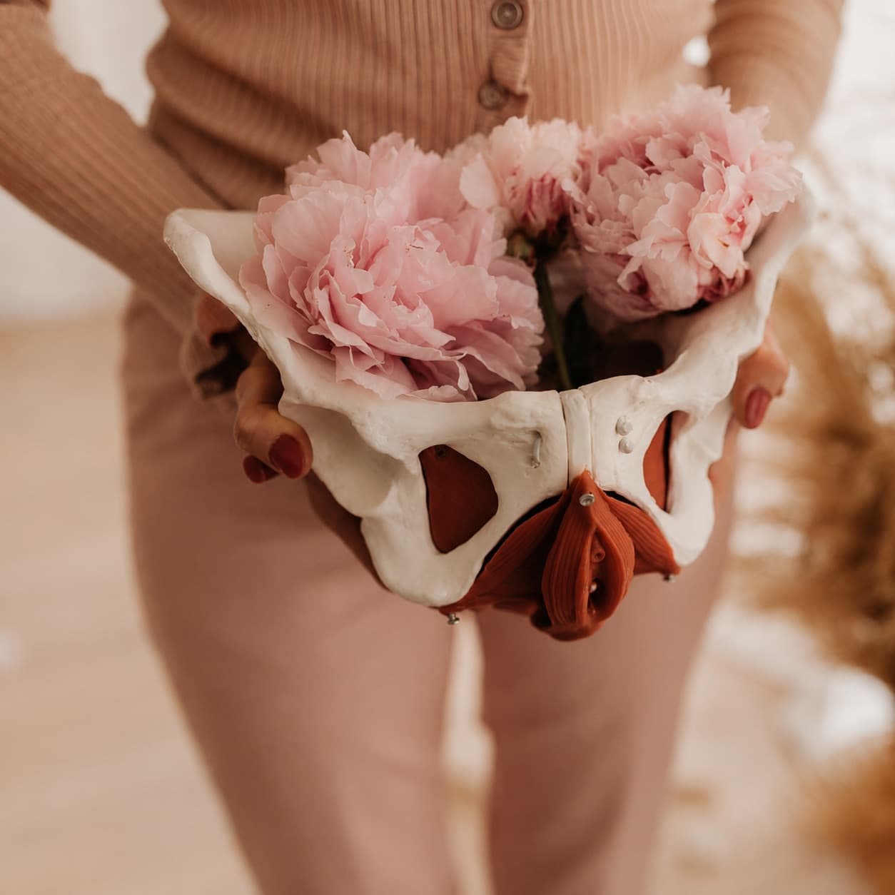 A woman holding an anatomical model of the female pelvis filled with peonies