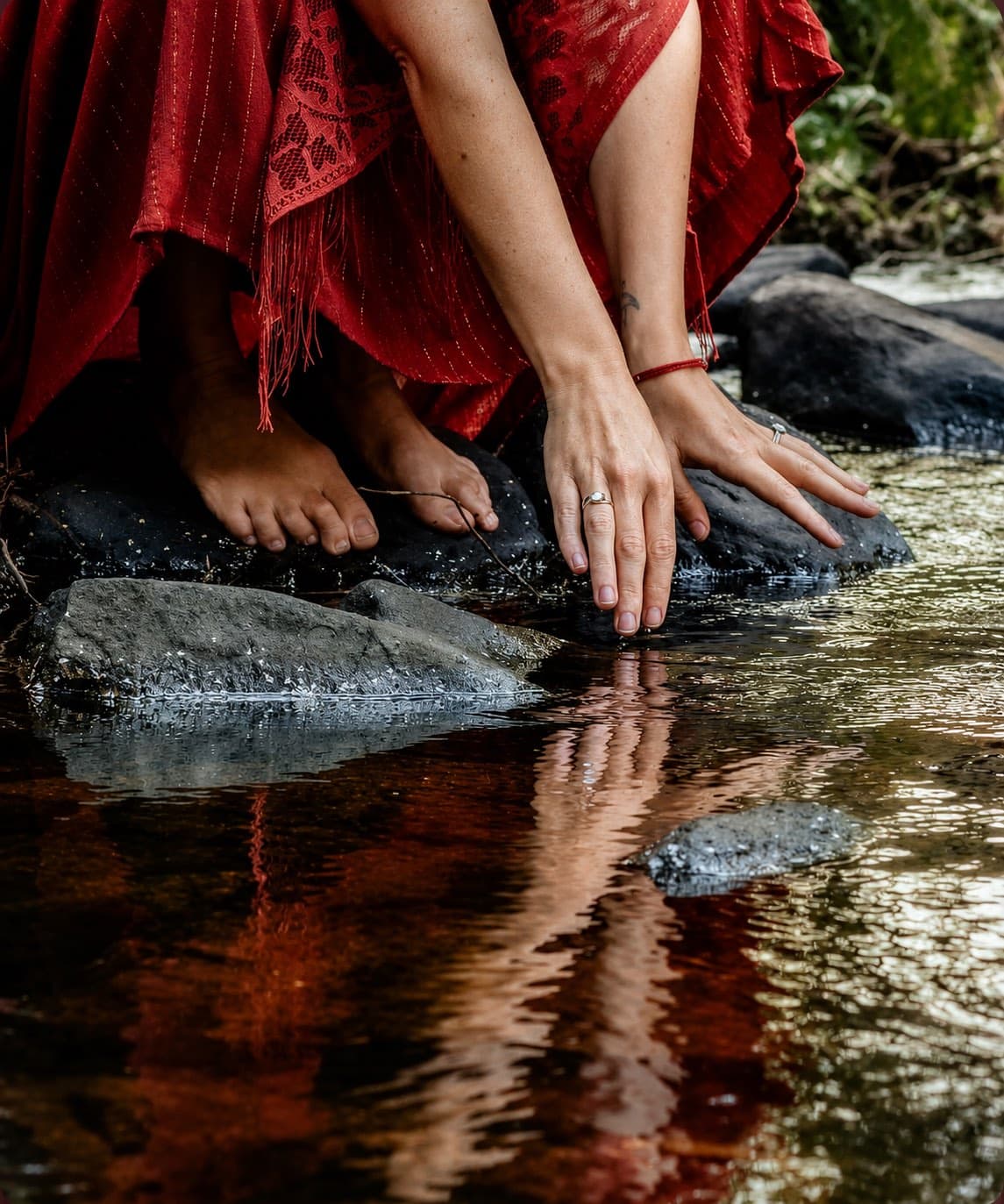 A woman in red kneeling at a river, her hands resting in the water