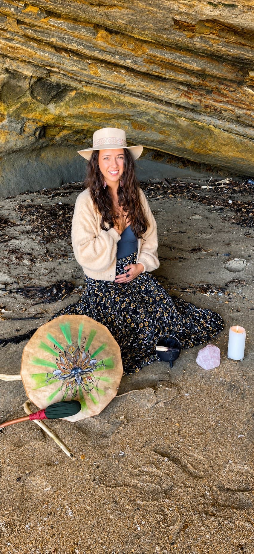 Sophia sitting on the sand beside her drum, candle and crystals