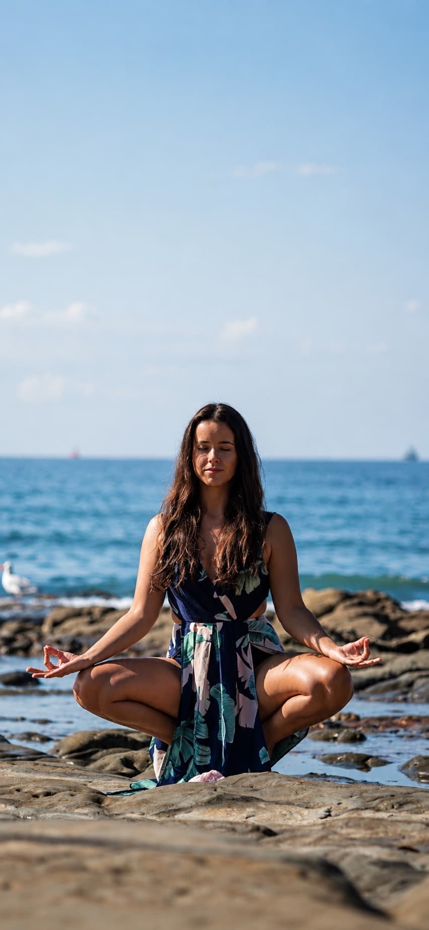 Sophia Cataldo sitting in meditation on the rocks above the sea