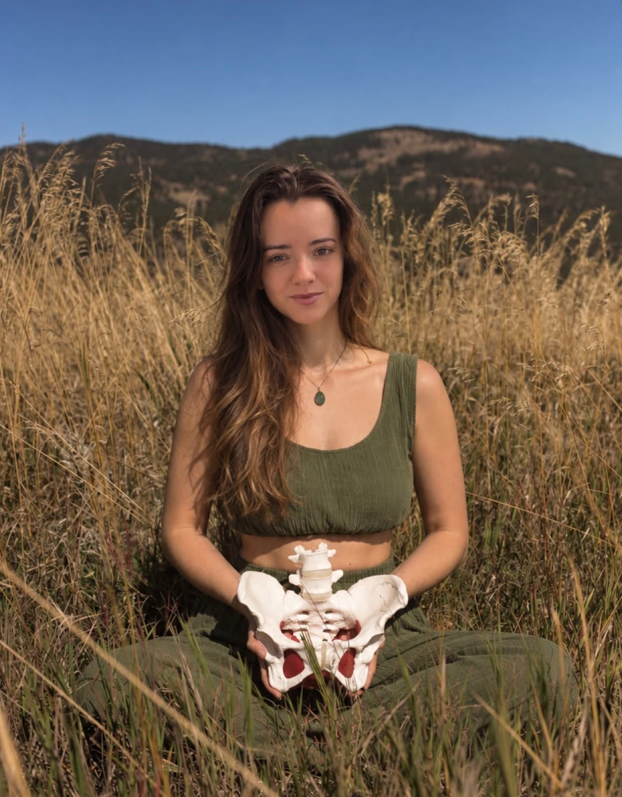 A woman holding an anatomical model of the female pelvis in a grassland
