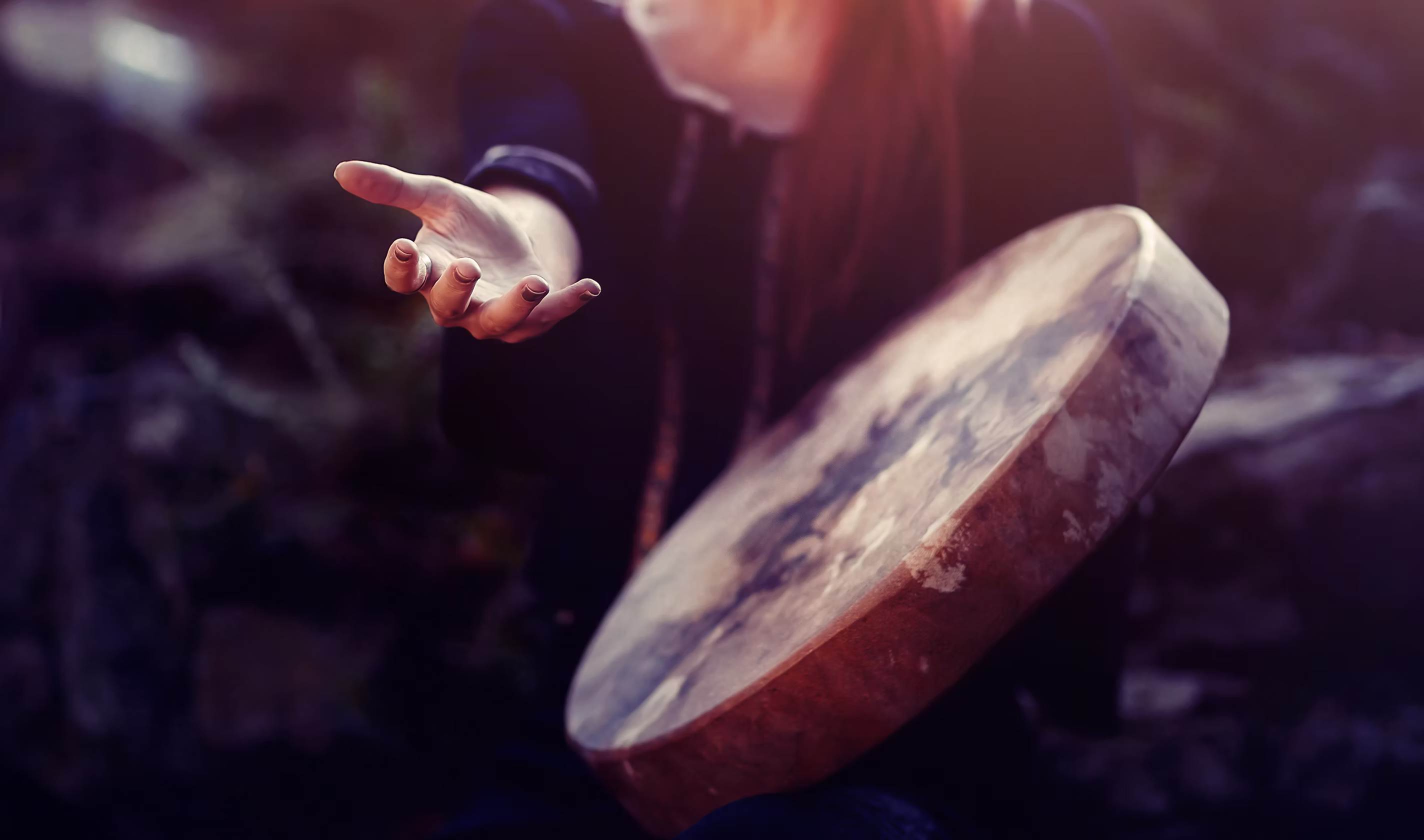 A hand holding a shamanic drum in moody light